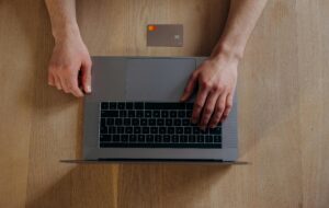 Top view of male hands on a laptop with credit card on wooden table, ideal for online shopping themes.